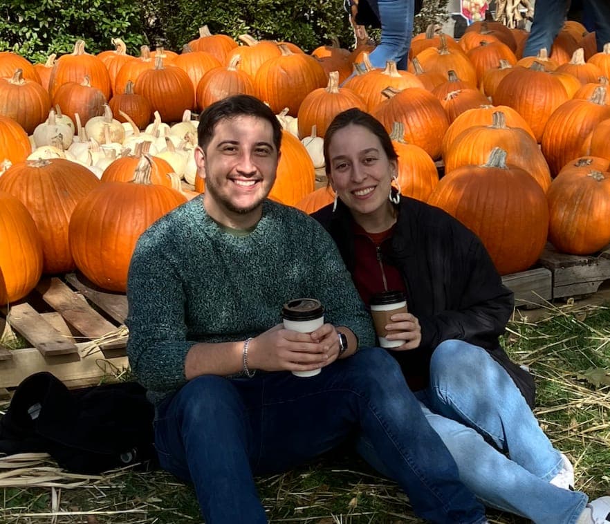 Mercedes and Michael with coffees, sitting in front of a pile of pumpkins